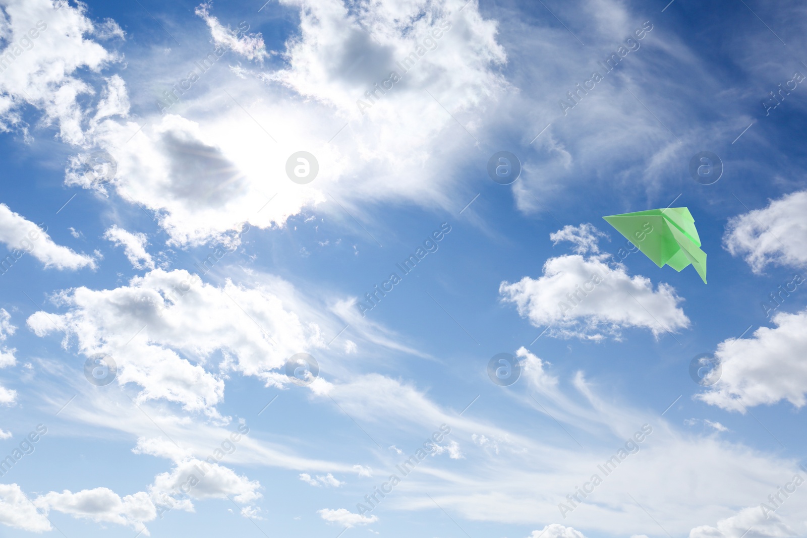 Image of Green paper plane flying in blue sky with clouds