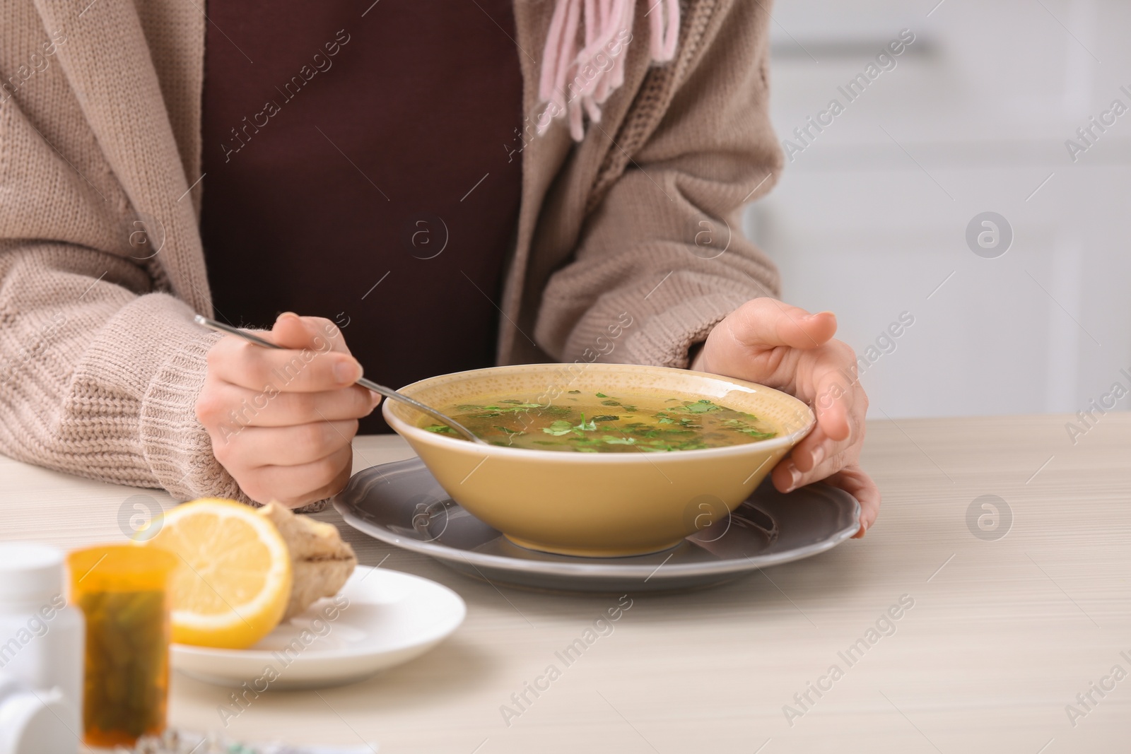 Photo of Sick young woman eating broth to cure cold at table in kitchen