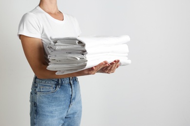 Woman holding stack of clean bed linens on light grey background