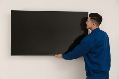 Photo of Professional technician installing modern flat screen TV on wall indoors