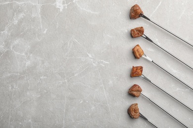 Forks with fried meat fondue pieces on grey background, top view. Space for text