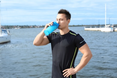 Photo of Young man drinking protein shake near river