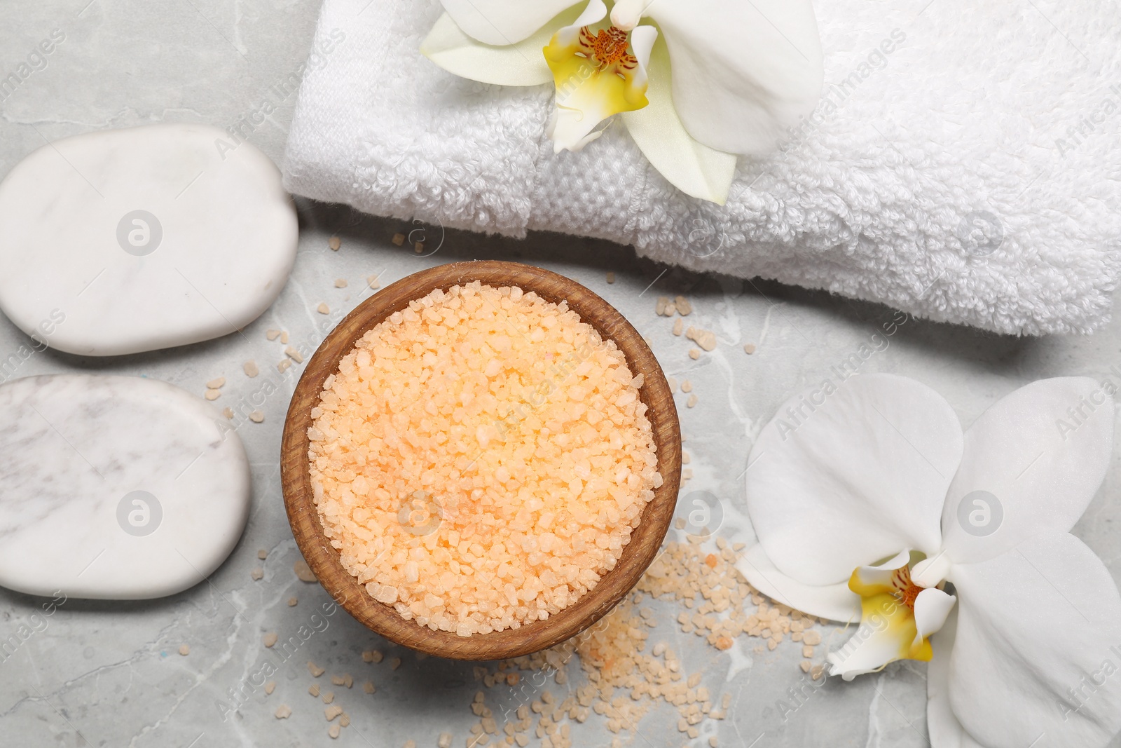 Photo of Orange sea salt in bowl, spa stones, towel and flowers on grey marble table, flat lay