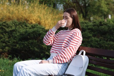 Photo of Woman with napkin suffering from seasonal allergy on bench in park