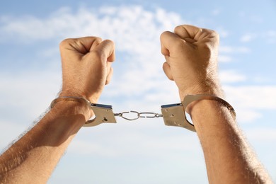 Photo of Man in handcuffs against blue sky outdoors, closeup