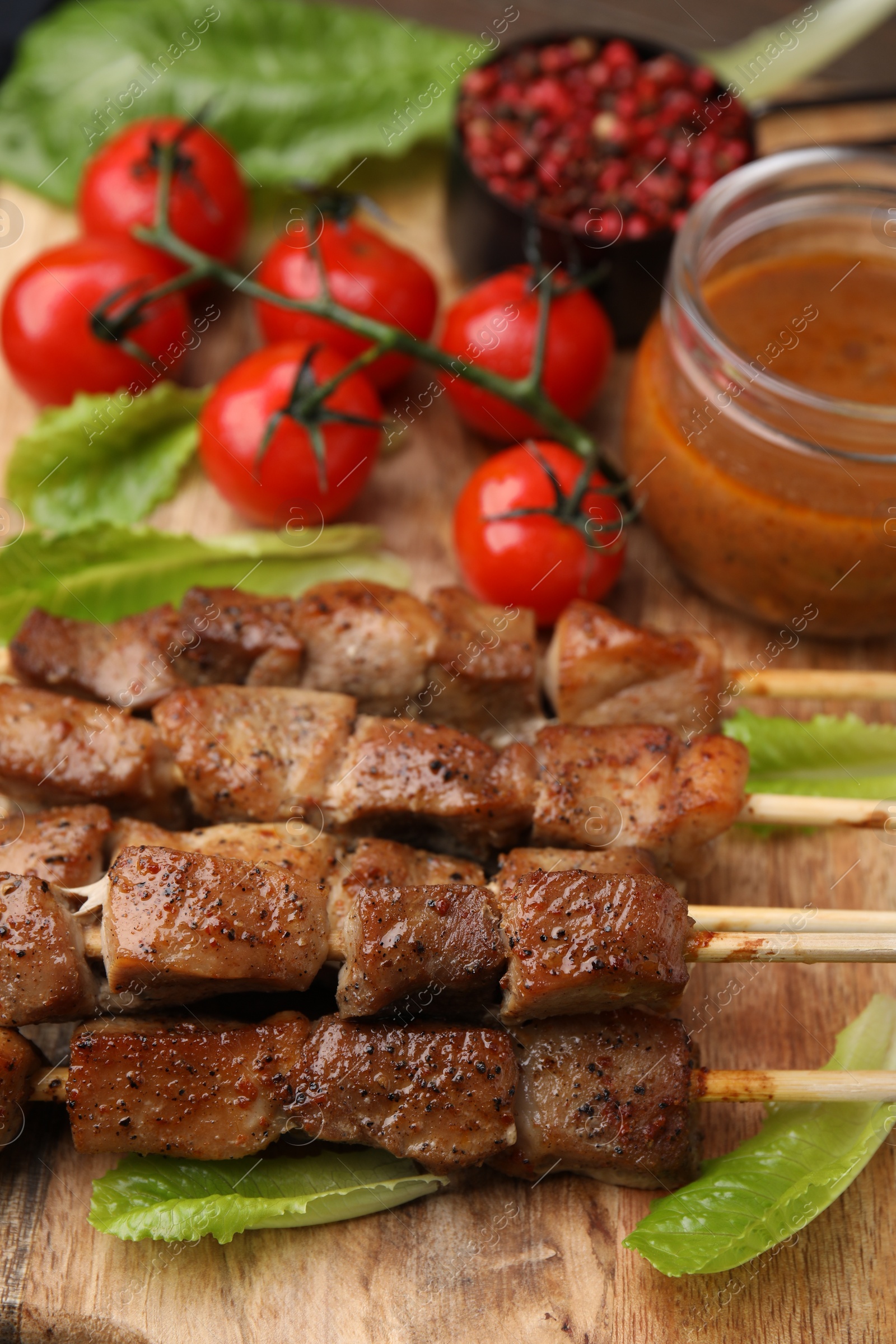 Photo of Tasty cooked marinated meat served with sauce and tomatoes on wooden table, closeup