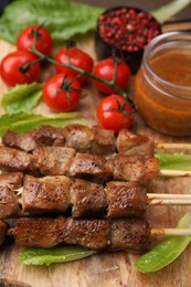 Photo of Tasty cooked marinated meat served with sauce and tomatoes on wooden table, closeup