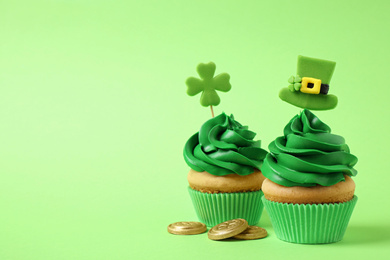 Delicious decorated cupcakes and coins on light green background, space for text. St. Patrick's Day celebration