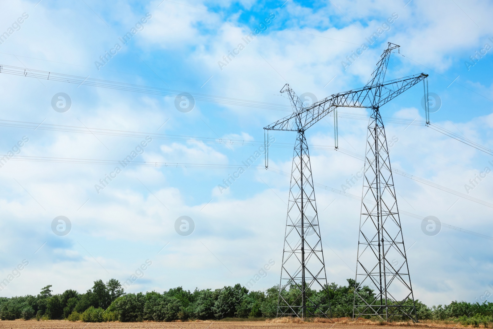 Photo of High voltage towers with electricity transmission power lines in field on sunny day