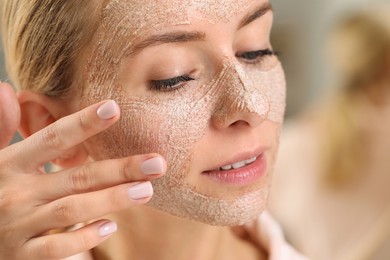 Woman applying face mask on blurred background, closeup. Spa treatments