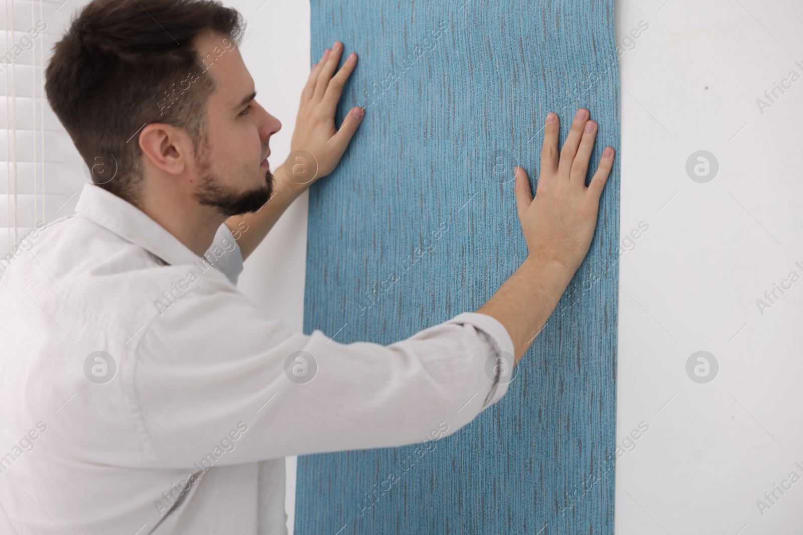 Photo of Man hanging light blue wallpaper in room