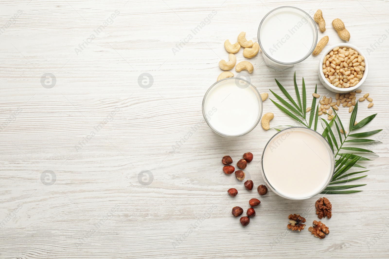 Photo of Different vegan milks and nuts on white wooden table, flat lay. Space for text
