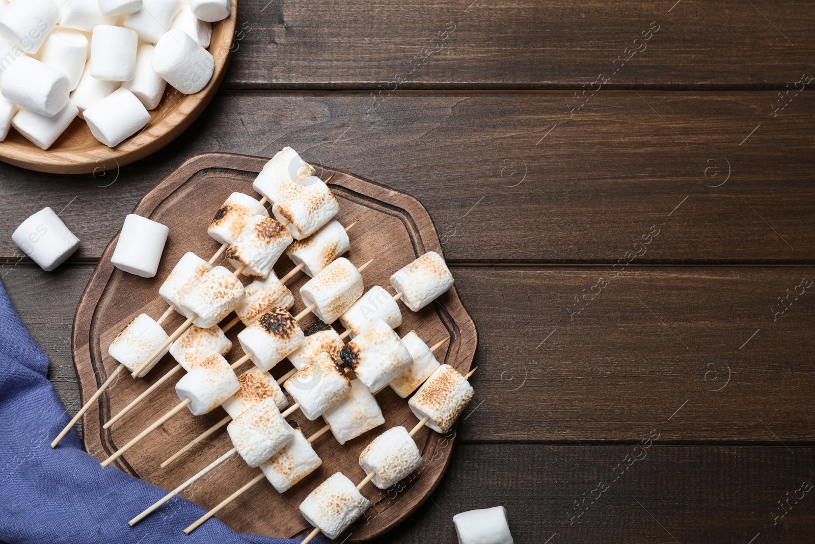 Photo of Sticks with roasted marshmallows on wooden table, flat lay. Space for text
