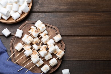 Sticks with roasted marshmallows on wooden table, flat lay. Space for text