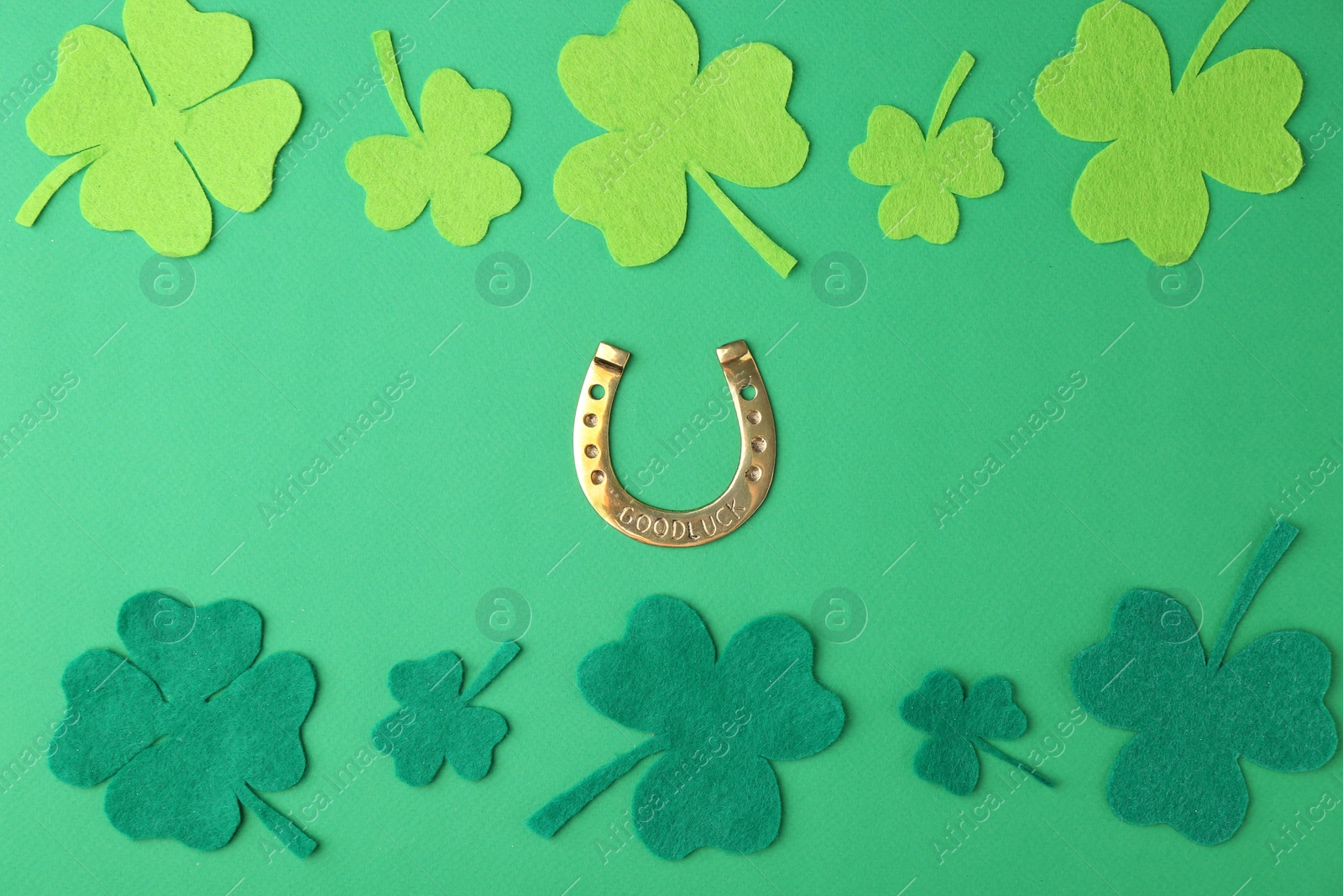 Photo of St. Patrick's day. Golden horseshoe and decorative clover leaves on green background, flat lay