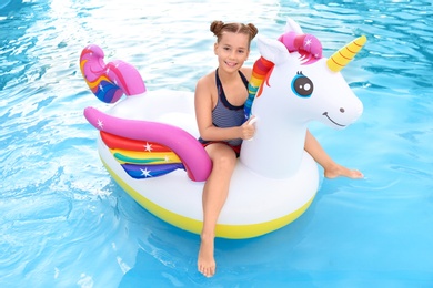 Photo of Happy little girl on inflatable unicorn in swimming pool