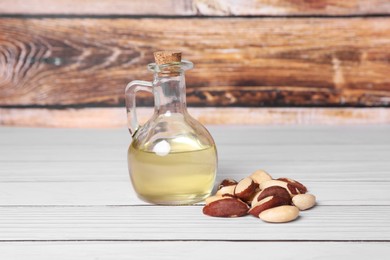 Photo of Tasty Brazil nuts and bottle with oil on white wooden table