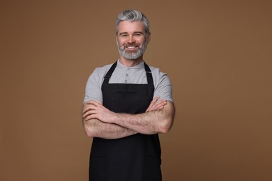 Photo of Happy man wearing kitchen apron on brown background. Mockup for design