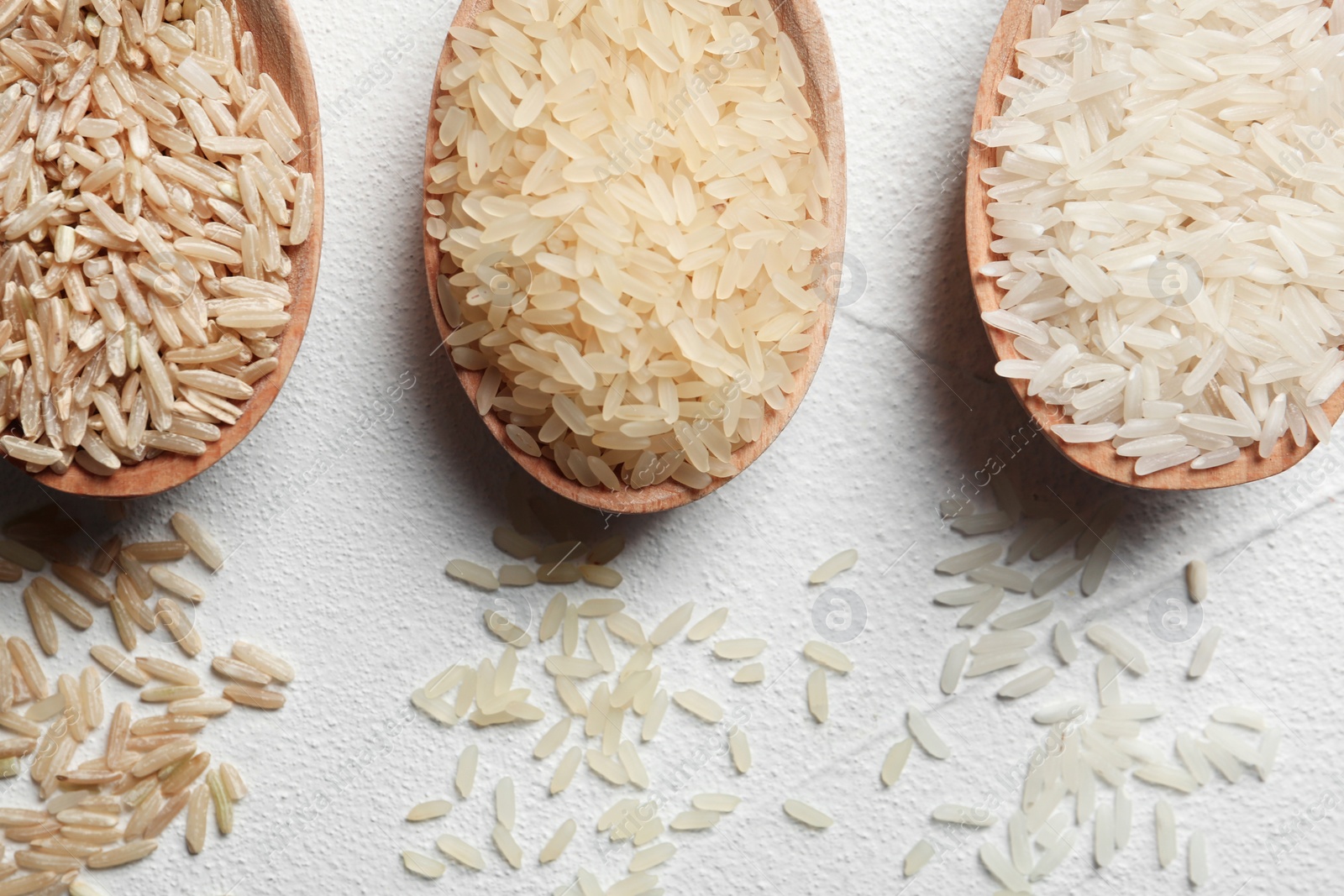 Photo of Flat lay composition with brown and other types of rice in spoons on white background