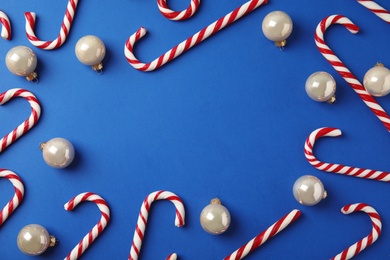 Photo of Flat lay composition with candy canes and Christmas balls on blue background. Space for text
