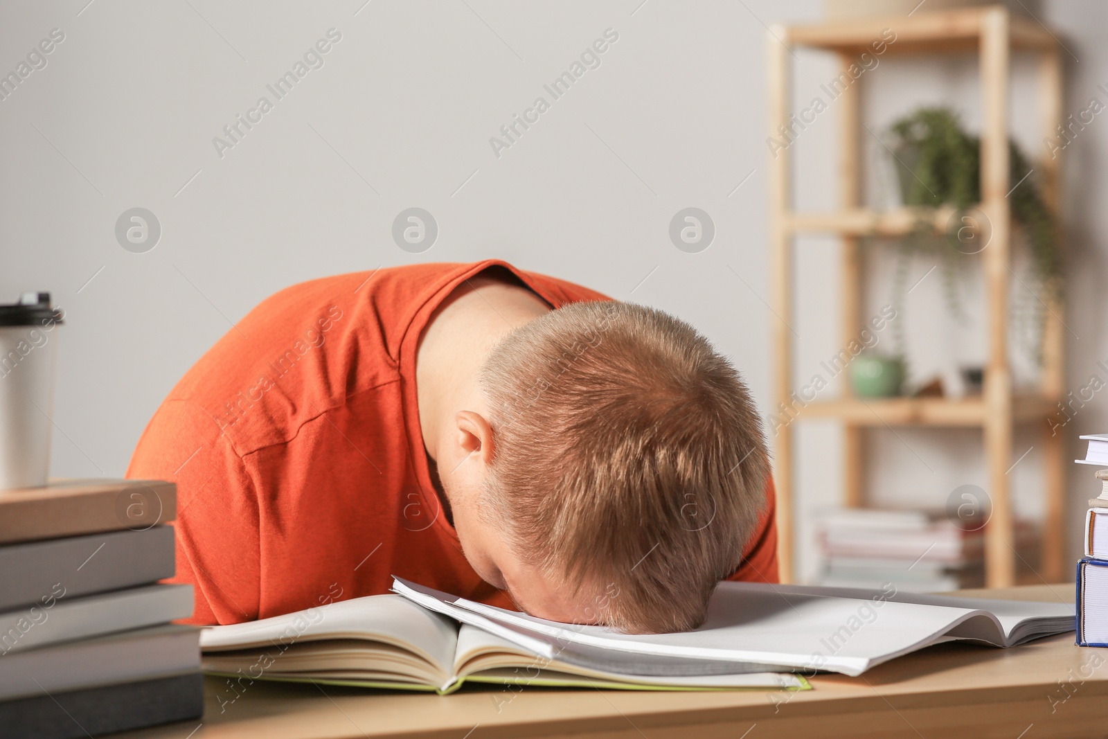 Photo of Tired man sleeping near books at wooden table indoors