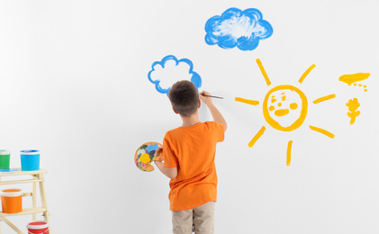 Little child painting cloud on white wall in room