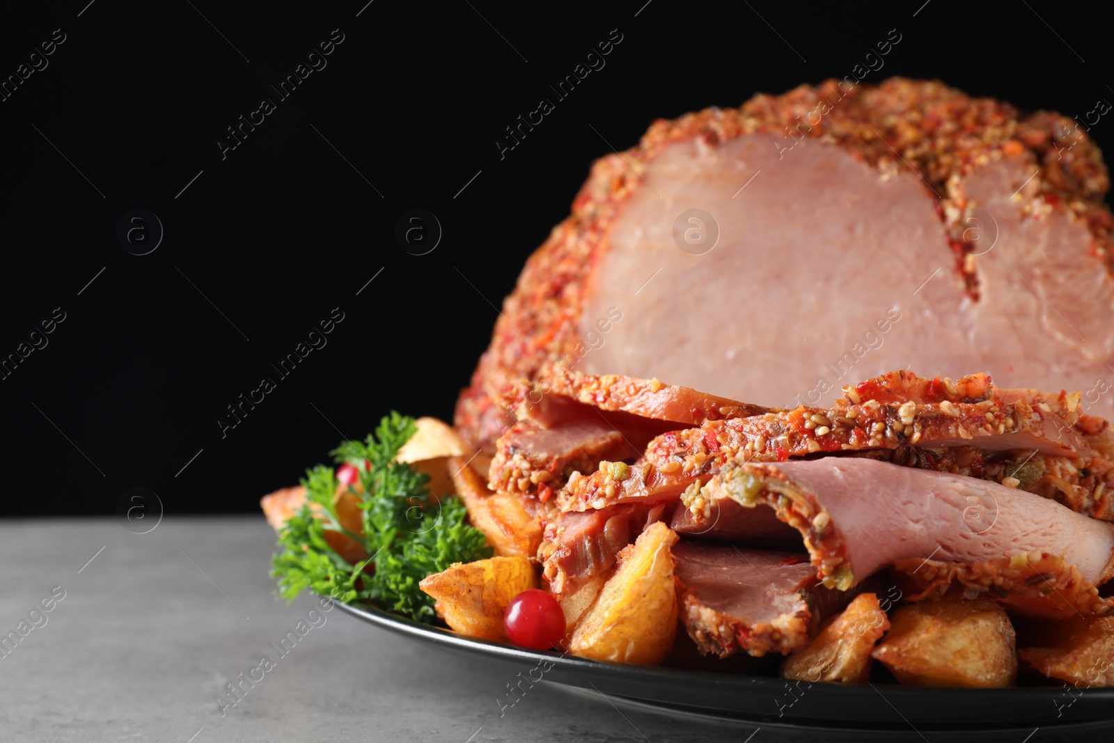 Photo of Plate with delicious ham and potatoes on grey table against black background, space for text