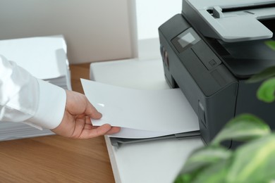 Photo of Woman loading paper into printer at wooden table indoors, closeup