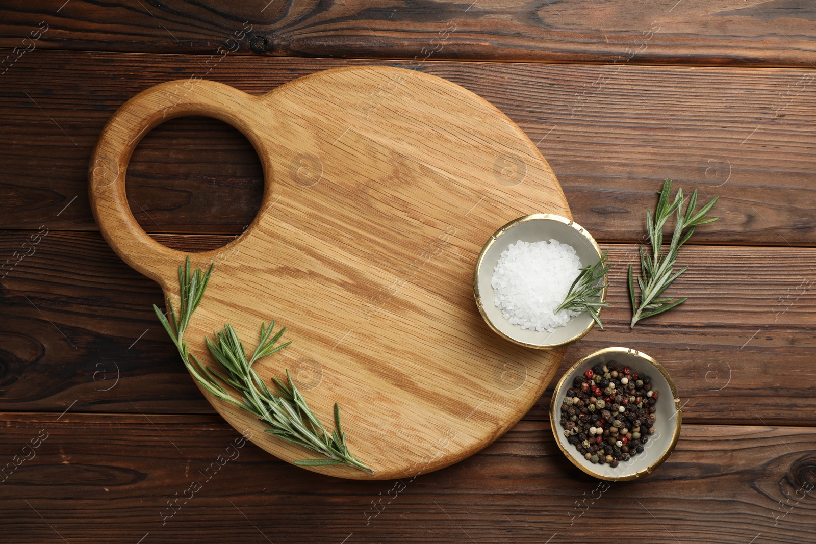 Photo of Cutting board, salt, pepper and rosemary on wooden table, flat lay. Space for text