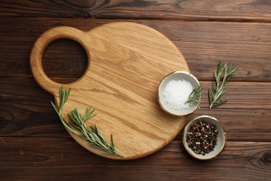 Photo of Cutting board, salt, pepper and rosemary on wooden table, flat lay. Space for text