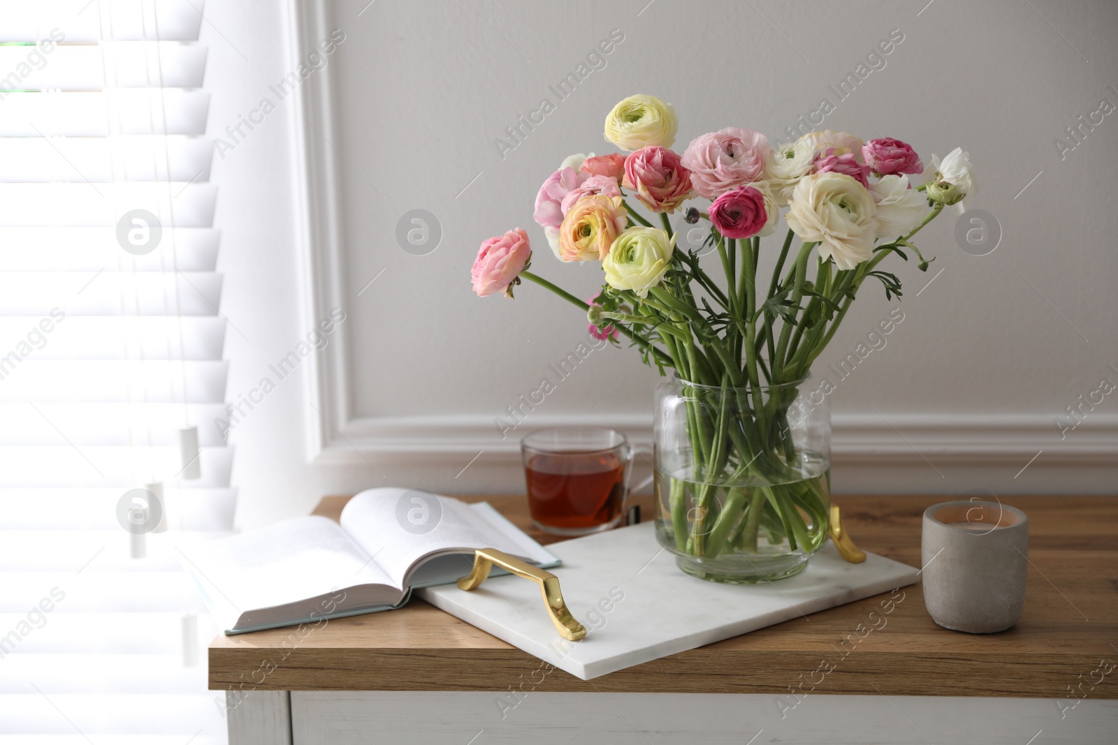Photo of Bouquet of beautiful ranunculuses, candle and tea on cabinet in room