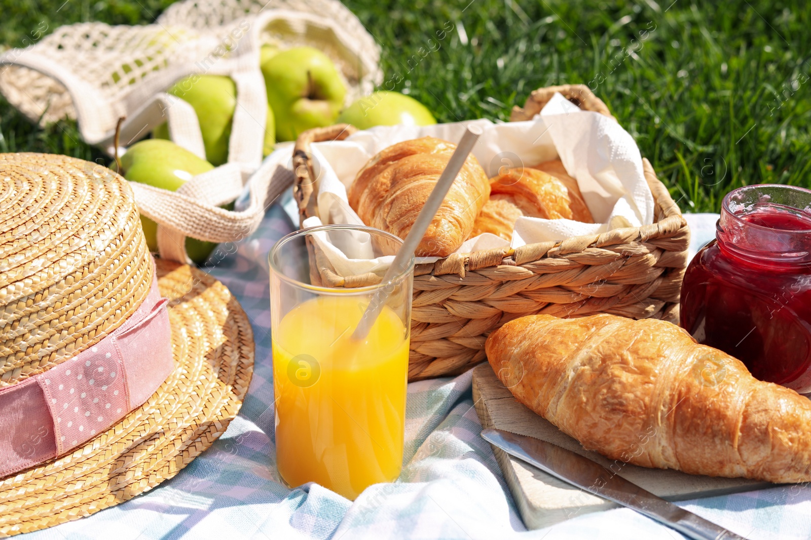 Photo of Blanket with juice, jam and croissants for picnic on green grass, closeup