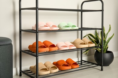 Shoe rack with different pairs of rubber slippers near white wall indoors