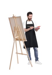 Artist with brush painting against white background. Using easel to hold canvas