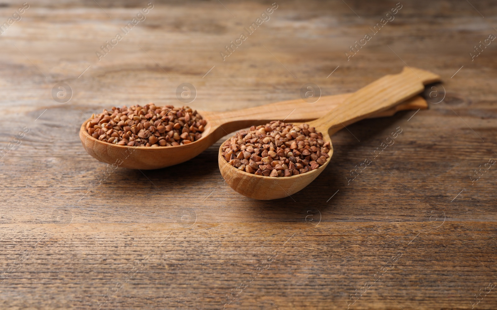 Photo of Buckwheat grains in spoons on wooden table