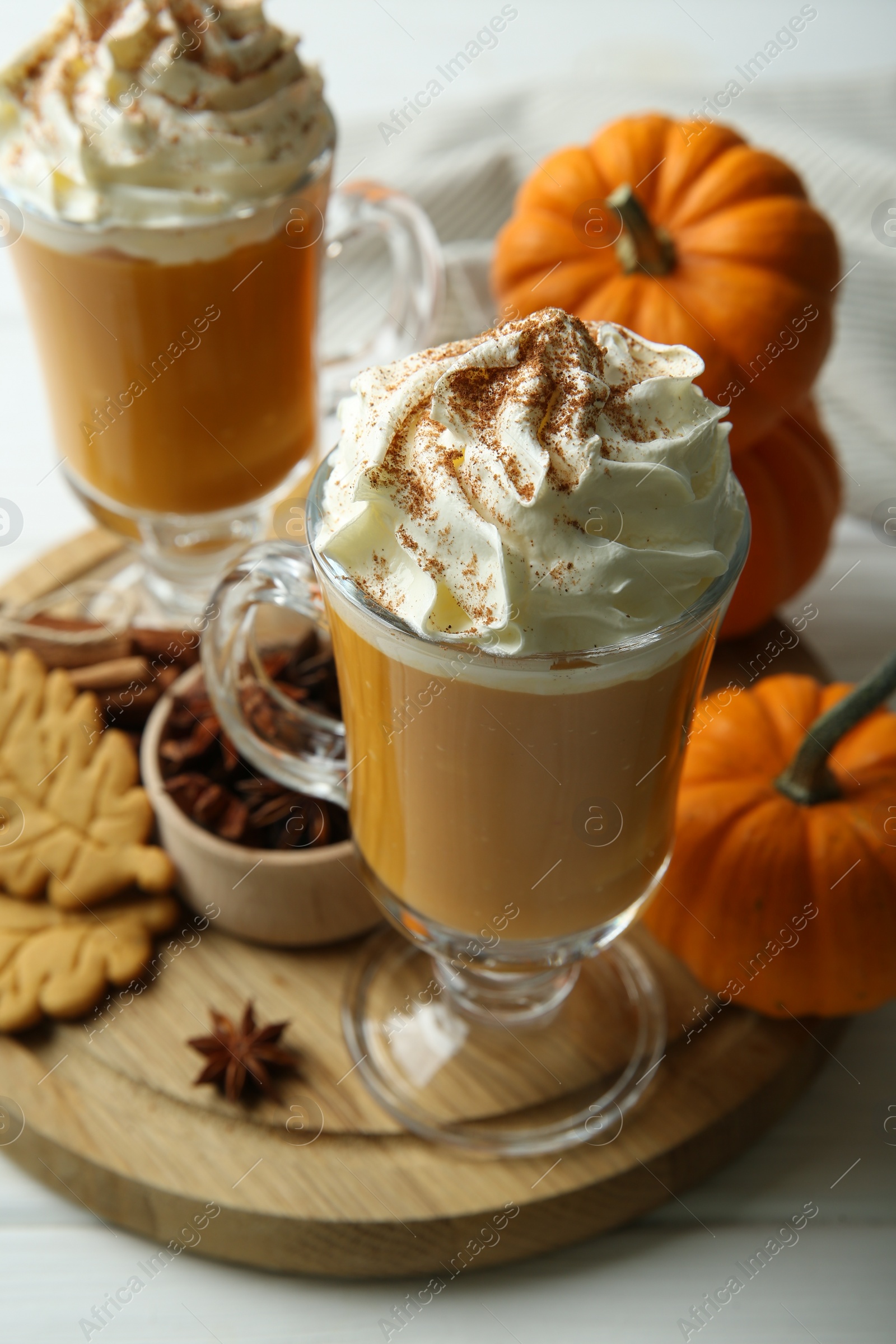 Photo of Tasty pumpkin latte with whipped cream in glasses, spices and cookies on white table, closeup