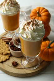 Photo of Tasty pumpkin latte with whipped cream in glasses, spices and cookies on white table, closeup