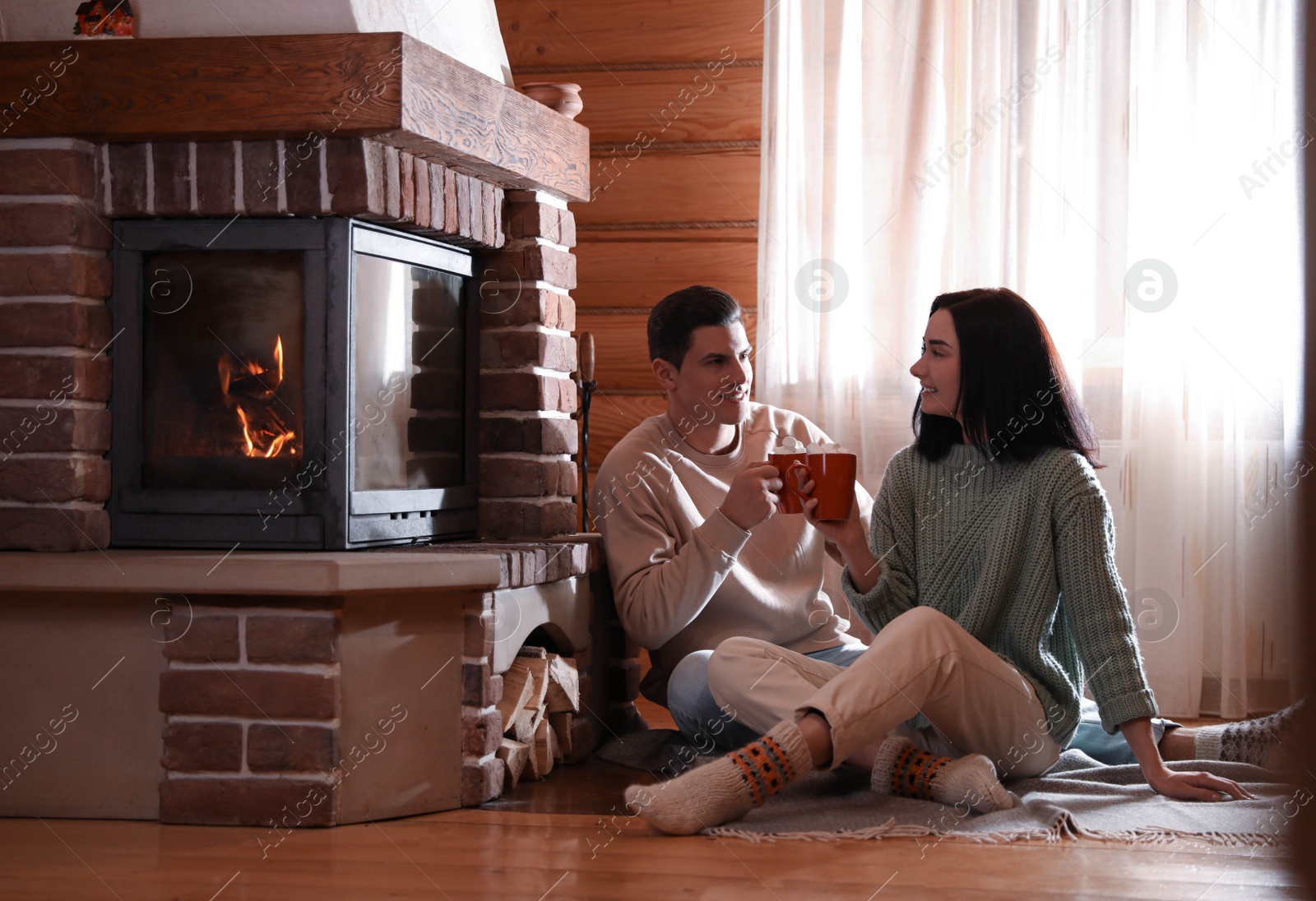 Photo of Lovely couple with delicious cocoa near fireplace on floor at home. Winter vacation