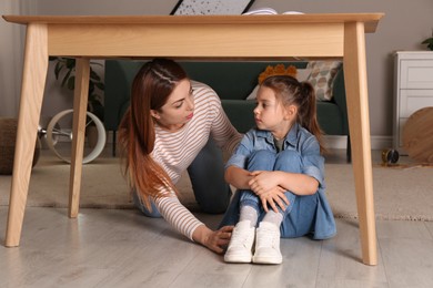 Photo of Scared mother with her little daughter hiding under table in living room during earthquake
