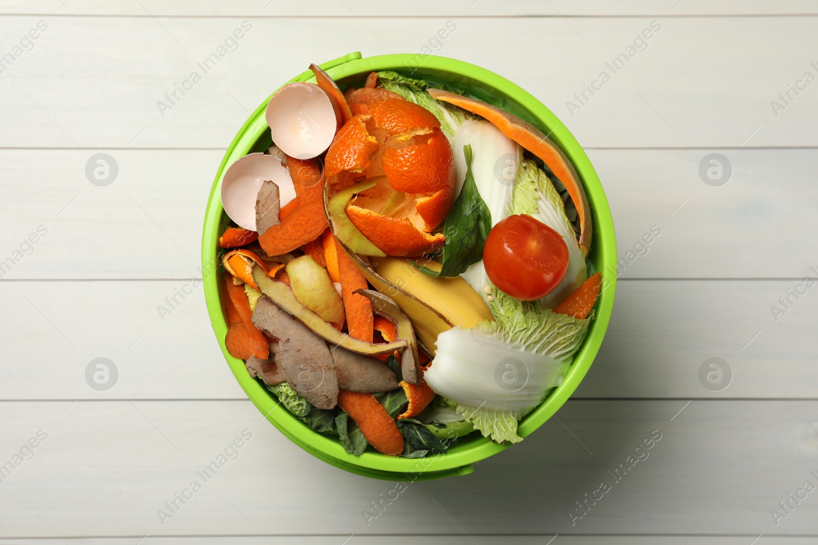 Photo of Trash bin with organic waste for composting on white wooden background, top view