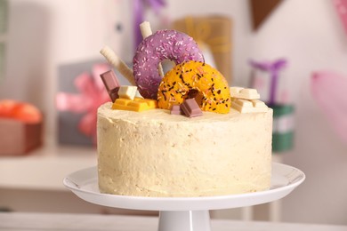 Photo of White stand with delicious cake decorated with sweets against blurred background, closeup