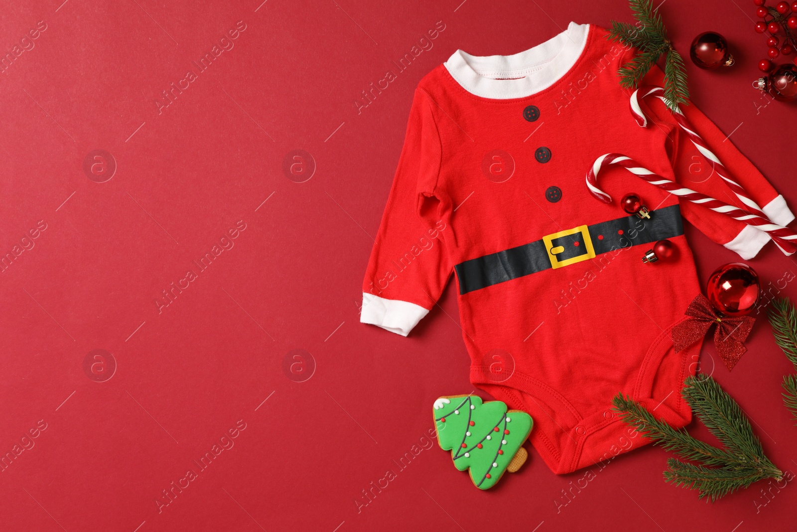 Photo of Flat lay composition with cute Christmas baby clothes on red background. Space for text