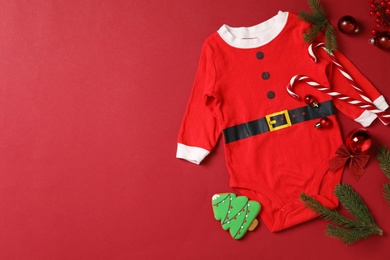 Photo of Flat lay composition with cute Christmas baby clothes on red background. Space for text