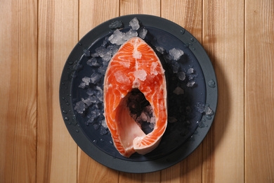 Fresh raw fish steak with ice on wooden table, top view