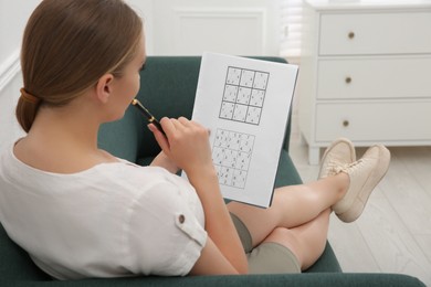 Photo of Young woman solving sudoku puzzle on sofa indoors