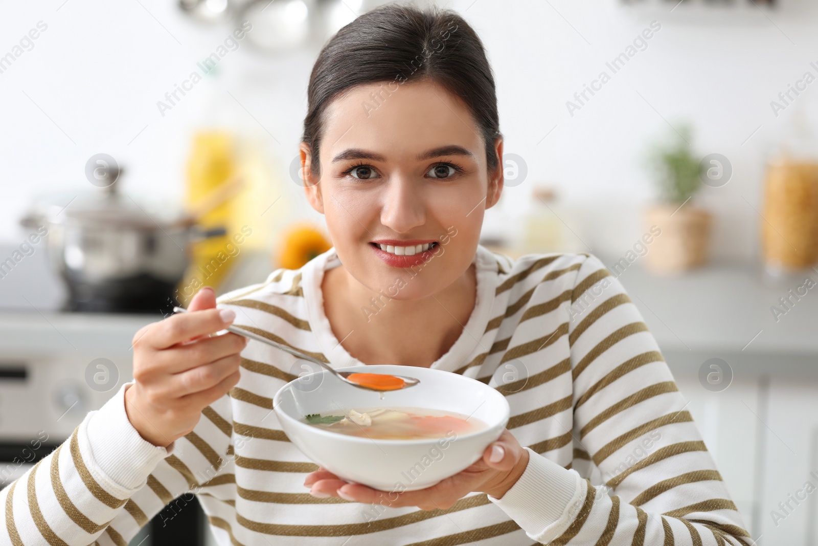 Photo of Young woman eating tasty vegetable soup indoors