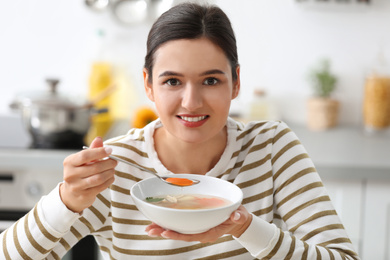 Photo of Young woman eating tasty vegetable soup indoors