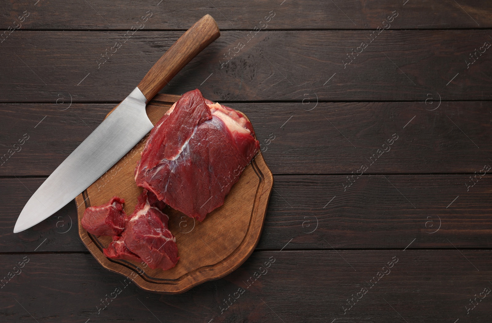 Photo of Pieces of raw beef meat and knife on wooden table, top view. Space for text