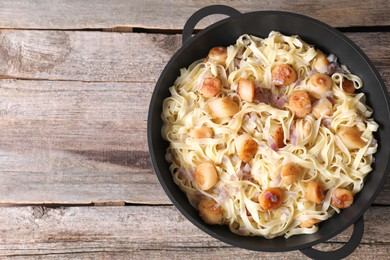 Photo of Delicious scallop pasta with onion in pan on wooden table, top view. Space for text