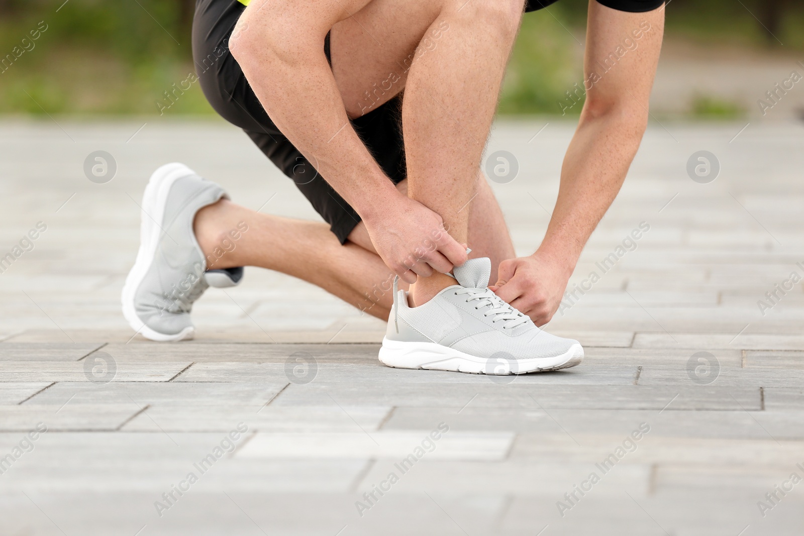 Photo of Young man tying shoelaces before running outdoors, focus on legs